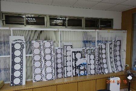 A collection of various engine cylinder head gaskets, featuring different sizes and hole patterns, arranged on a wooden surface in what appears to be a workshop or storage area.