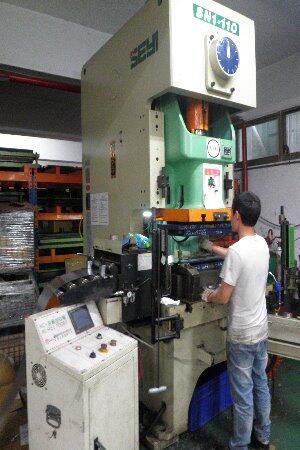 A person operates a large industrial SEYI SN1-110 Stamping Machine in a workshop, with metal shelving and other equipment visible in the background, depicting an industrial manufacturing scene.