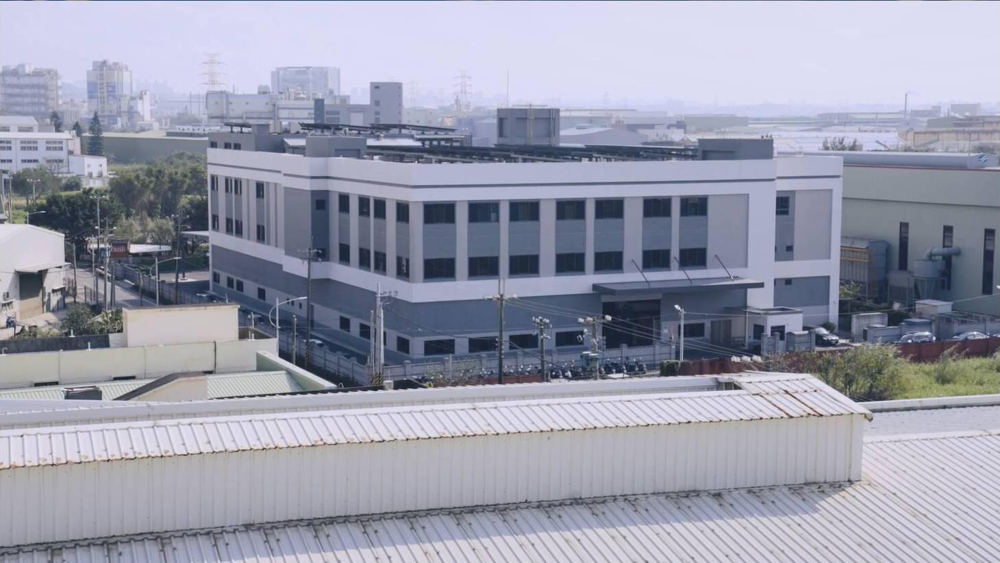 Exterior view of a contemporary multi-story industrial or factory building in an urban or industrial area in Taiwan, featuring a grey and white facade with prominent windows.