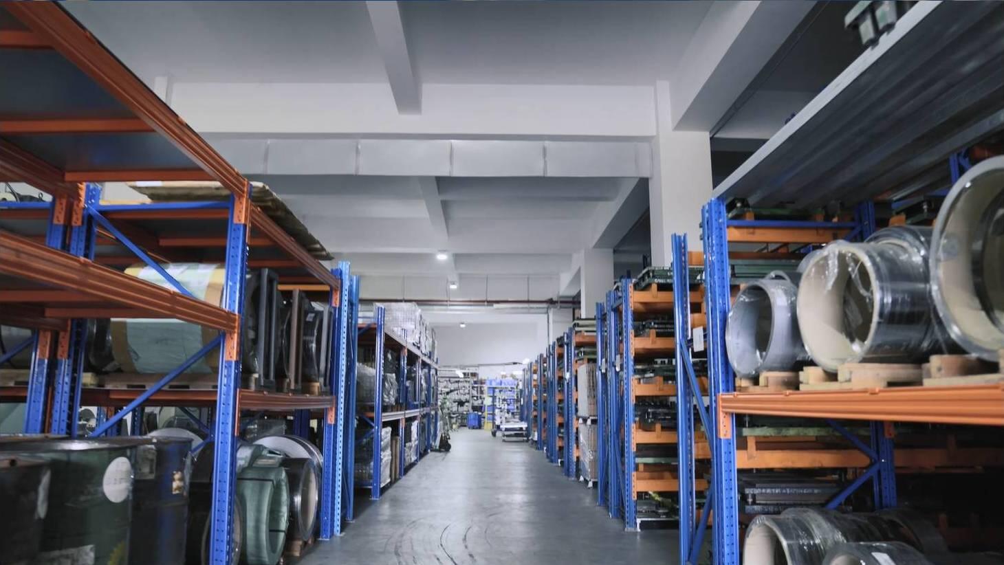 Long view of a well-organized warehouse aisle with tall, blue and orange metal shelving units filled with various industrial materials and products, creating a sense of order and large-scale storage.
